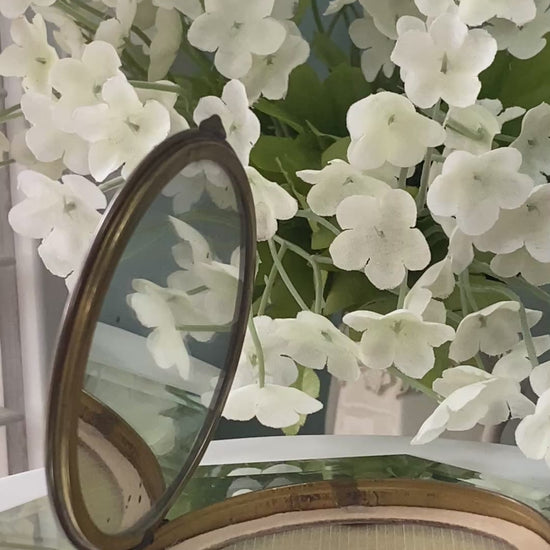 vintage compact on a reflective surface with flowers in the background
