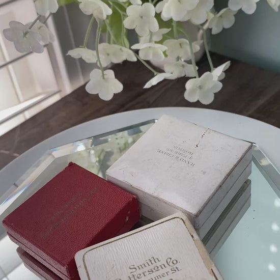antique jewelry boxes on a reflective surface with flowers in the background